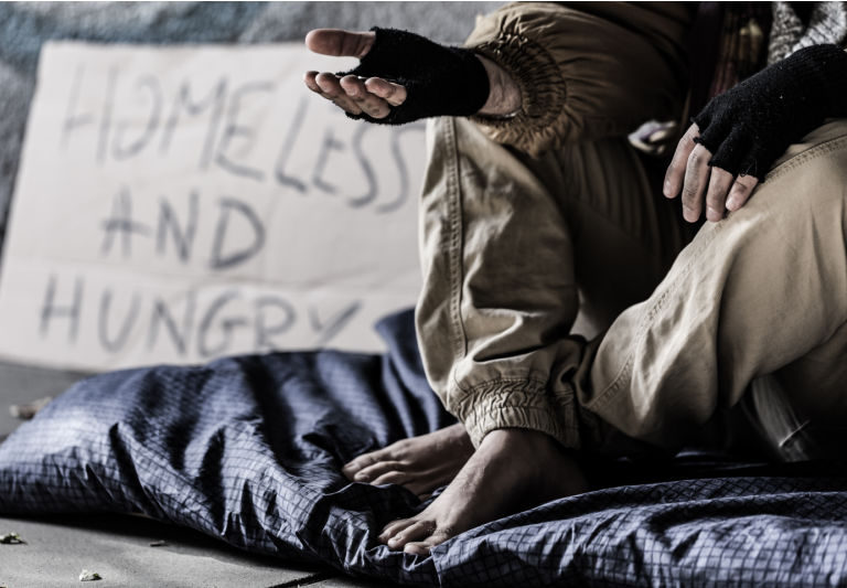 Close-up of dirty and barefoot street person sitting on a blanket and begging