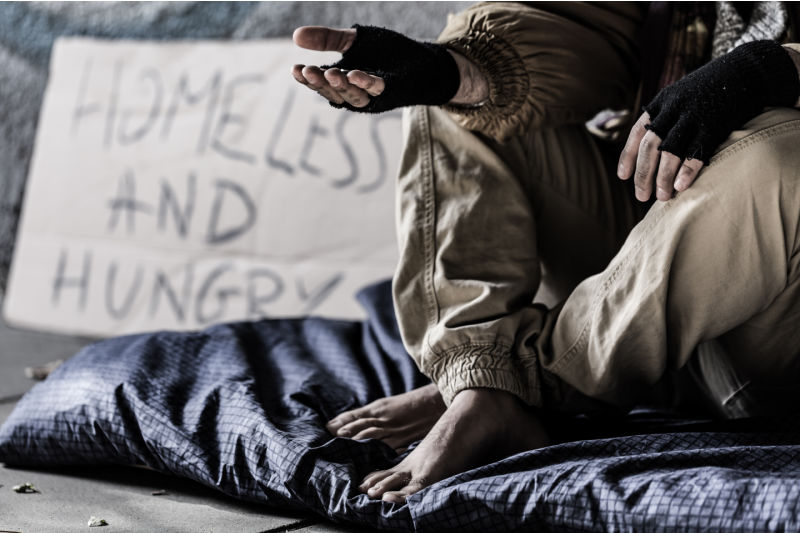 Close-up of dirty and barefoot street person sitting on a blanket and begging